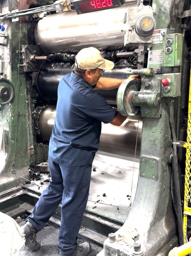 Factory worker operating an industrial rubber mixing or rolling machine.